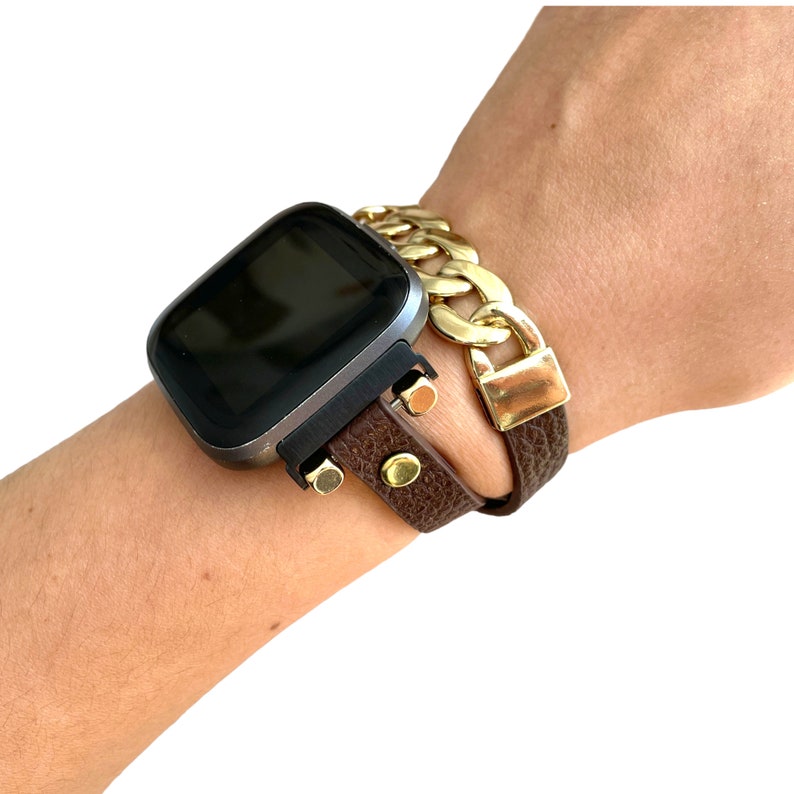Peut inclure: Un bracelet de montre en cuir marron avec un bracelet en cha&icirc;ne dor&eacute;e sur le dessus. Le bracelet de montre a des accents dor&eacute;s et est port&eacute; au poignet.