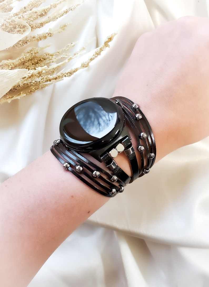 May include: A black smartwatch with a black leather band with silver beads. The band is wrapped around the wrist multiple times.