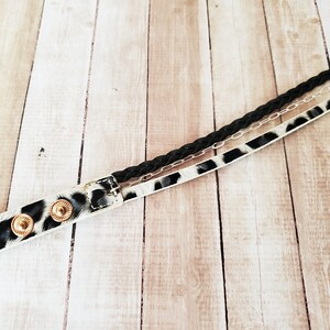 May include: A black braided cord, a silver chain, and a white and black leopard print leather strap are woven together to create a unique bracelet. The bracelet has gold-toned metal accents.