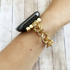 May include: A gold chain watch band with a black smartwatch. The band is made of thick, linked chains with a textured finish.