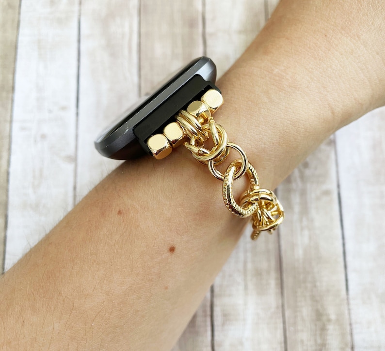 May include: A gold chain watch band with a black smartwatch. The band is made of thick, linked chains with a textured finish.