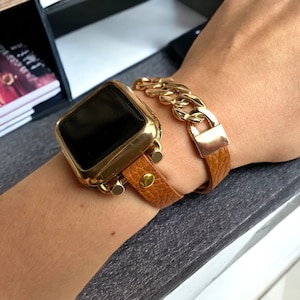 May include: A gold-tone watch with a brown leather band and a gold chain bracelet. The watch face is black and the band has a textured finish.