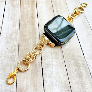 May include: A gold chain watch band with a black square watch face. The band is made of interlocking circles.