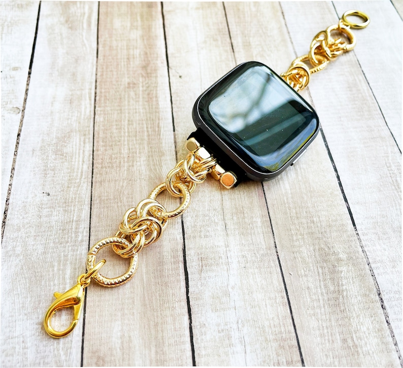 May include: A gold chain watch band with a black square watch face. The band is made of interlocking circles.