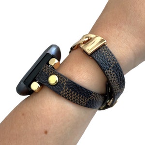 Peut inclure: Un bracelet de montre &agrave; motif noir et marron avec des accents dor&eacute;s. Le bracelet est enroul&eacute; autour d'un poignet.