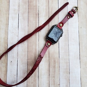 Może przedstawiać: Czerwony sk&oacute;rzany pasek do zegarka z misternym wzorem kwiatowym. Pasek jest przymocowany do czarnego Apple Watch.