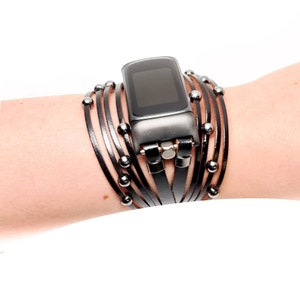 Puede incluir: Una pulsera de reloj de cuero negro con cuentas plateadas y un rastreador de fitness negro.
