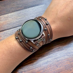 May include: A brown leather watch band with silver accents and metal studs. The band is wrapped around a wrist multiple times.