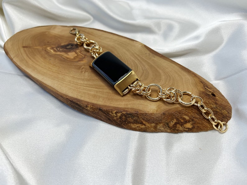 May include: A gold chain bracelet with a black rectangular charm. The bracelet is on a wooden surface.