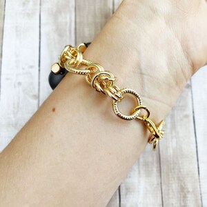 May include: A gold chain bracelet with a chunky, textured design. The bracelet is made of thick, linked chains with a clasp closure.
