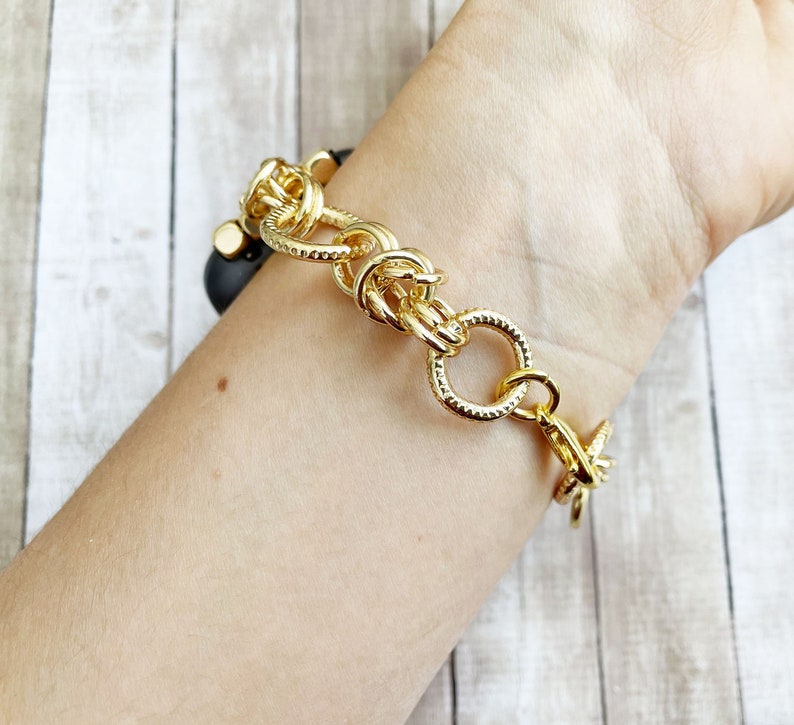 May include: A gold chain bracelet with a chunky, textured design. The bracelet is made of thick, linked chains with a clasp closure.
