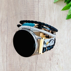 K&ouml;nnte beinhalten: Eine silberne Smartwatch mit schwarzem Bildschirm wird mit einem mehrschichtigen Armband kombiniert. Das Armband hat geflochtenes schwarzes Leder, silberne Perlen, goldene Akzente und ein Schlangenmuster.