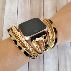 May include: A rose gold Fitbit smartwatch with a black band and a leopard print and gold chain bracelet.