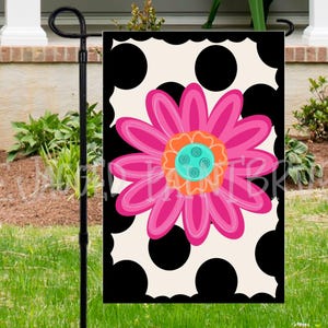 May include: A decorative garden flag featuring a large pink flower with orange and teal accents, set against a black and cream polka dot background. The flag is designed for outdoor use and adds a pop of color to any garden or yard.