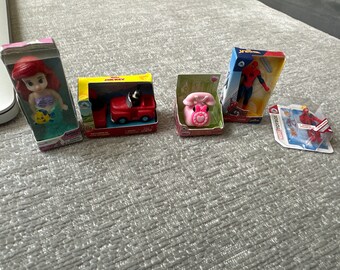 May include: A collection of miniature toys in their original packaging. Includes a Disney's Ariel doll, a Mickey Mouse red truck, a pink telephone, a Spider-Man action figure, and a Deadpool action figure.
