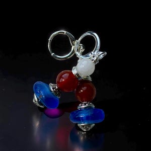 May include: A pair of earrings featuring a silver clasp and a design of red, white, and blue beads. The earrings have a patriotic color scheme with a mix of round and flattened beads.