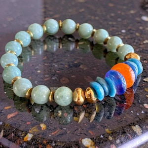 May include: A beaded bracelet featuring light green, round beads separated by gold-colored spacers. The bracelet includes a section of blue, orange, and purple beads. The bracelet is a piece of jewelry.