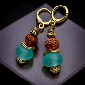 May include: Gold-tone earrings with a lever back closure. Each earring features a teal-colored glass bead, a brown bead, and gold-colored decorative elements. The earrings are displayed on a dark surface.