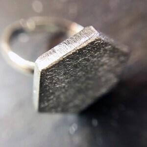 May include: A silver ring with a hexagonal shaped top. The ring is made of metal and has a brushed finish.