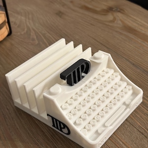 May include: White plastic typewriter-shaped desk organizer with black lettering. The organizer has slots for holding papers or cards. The word "TIP" is printed on the side of the organizer.