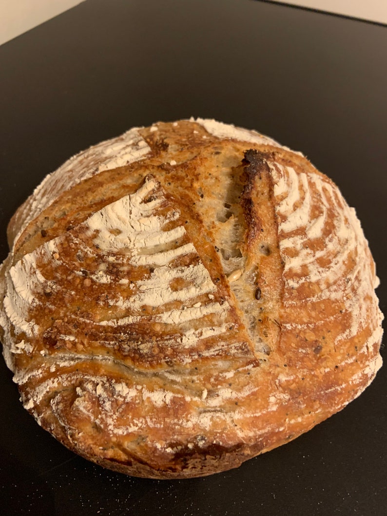 K&ouml;nnte beinhalten: Ein frisch gebackenes Sauerteigbrot mit einer knusprigen Kruste und einer leichten Mehlbest&auml;ubung. Das Brot hat ein rustikales Aussehen mit einem tiefen Einschnittmuster.