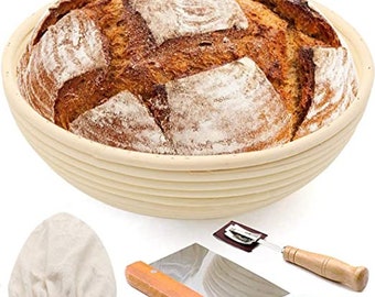 May include: A round, woven,  basket made of natural, light brown rattan, with a loaf of freshly baked bread inside. The basket is used for proving bread dough. The image also includes a dough scraper, a linen cloth, and a razor blade.