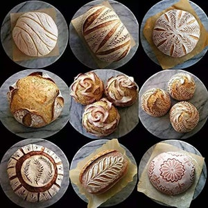 May include: Nine different loaves of bread with various decorative patterns carved into the top crust. The loaves are arranged on white parchment paper on top of round, grey surfaces.