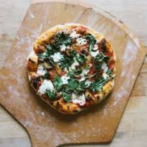 K&ouml;nnte beinhalten: Eine Pizza mit d&uuml;nnem Boden, belegt mit Tomatensauce, Mozzarella, Pilzen und frischen Kr&auml;utern. Die Pizza liegt auf einem Holzbrett.