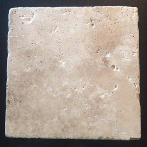 May include: A square, beige travertine tile with a rough, porous surface. The tile has a natural, earthy appearance, with variations in colour and texture. The edges are slightly uneven, adding to its rustic charm. The tile is suitable for various home decor projects.