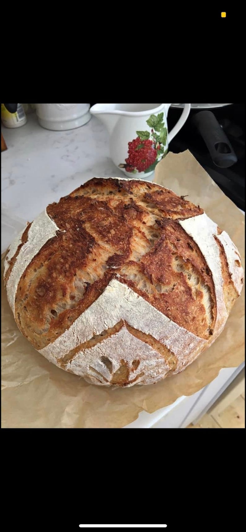 K&ouml;nnte beinhalten: Ein frisch gebackenes Sauerteigbrot mit einer knusprigen braunen Kruste und einem wei&szlig;en Inneren. Das Brot hat ein dekoratives Muster auf der Oberseite.