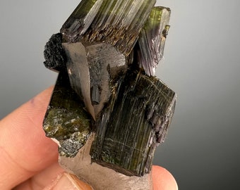 May include: A cluster of green and black crystals on a clear quartz point. The crystals are sharp and have a striated texture.