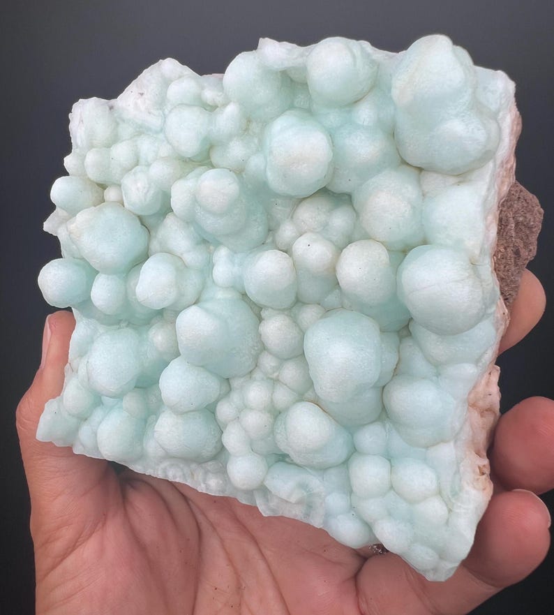 Op de afbeelding: Een groot, lichtblauw, bubbelvormig mineraalspecimen met een ruw, getextureerd oppervlak.