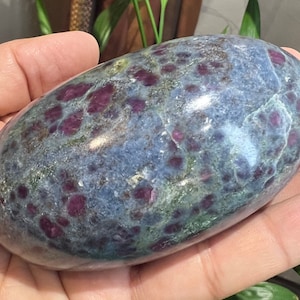 Puede incluir: Una piedra preciosa pulida, de forma ovalada y lisa, con un patrón moteado azul, verde y rojo. La piedra es una mezcla de azul y verde con motas rojas por todas partes.
