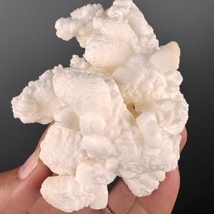 Op de afbeelding: Een groot, wit, bloemkoolachtig mineraalspecimen met een ruw, getextureerd oppervlak.