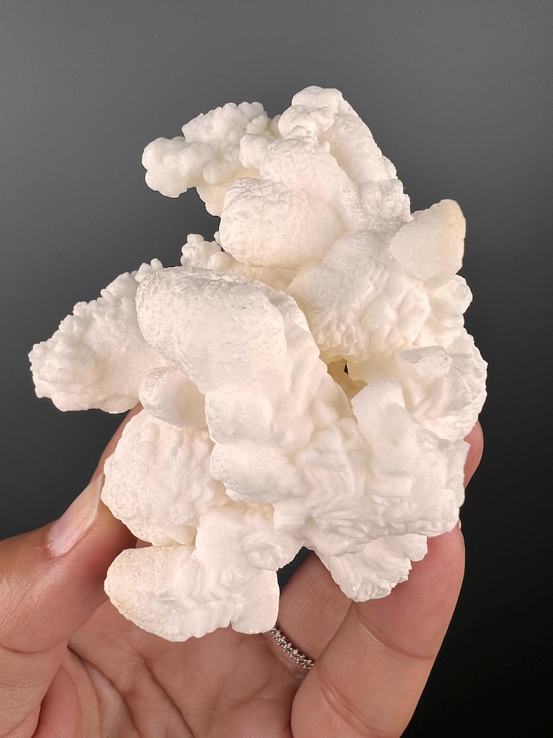 Op de afbeelding: Een groot, wit, bloemkoolachtig mineraalspecimen met een ruw, getextureerd oppervlak.