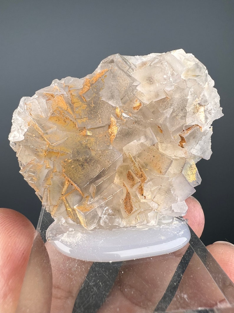 May include: A cluster of clear, faceted crystals with a golden hue. The crystals are arranged in a random pattern and have a rough, natural texture.