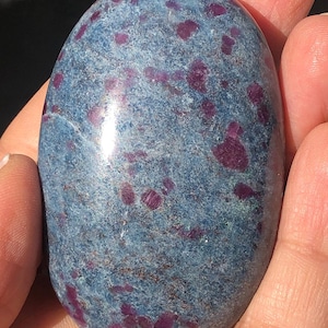 Op de afbeelding: Een gladde, ovale blauwe en paarse edelsteen met een gevlekt patroon. De edelsteen is gepolijst en heeft een glanzende afwerking.