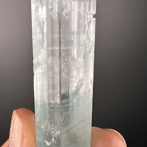 May include: A light blue aquamarine crystal with a faceted, rectangular shape. The crystal is translucent and has a slight green hue.