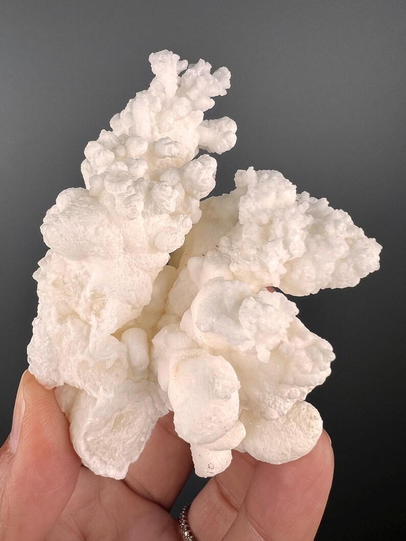 Op de afbeelding: Een cluster van witte, bloemkoolachtige mineraalformaties. Het mineraal heeft een ruw, getextureerd oppervlak.