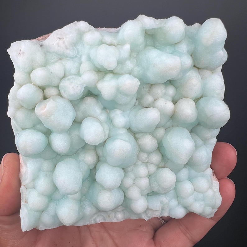 Op de afbeelding: Een lichtblauw, bubbelig en getextureerd mineraalmonster. Het mineraal heeft een glad, afgerond oppervlak met verschillende maten en vormen.