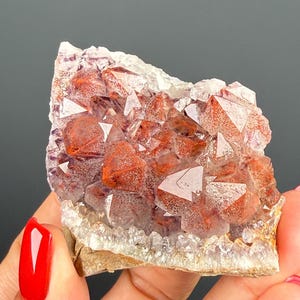 May include: A cluster of translucent quartz crystals featuring prominent reddish-brown inclusions within the points. The mineral specimen displays a jagged, natural formation with a light-coloured base and sharp, multifaceted crystal terminations.