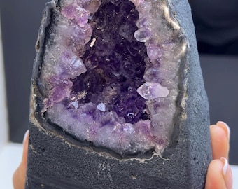 May include: A large amethyst geode with a deep purple interior and a black exterior. The geode is shaped like a triangle and has a smooth, polished surface.