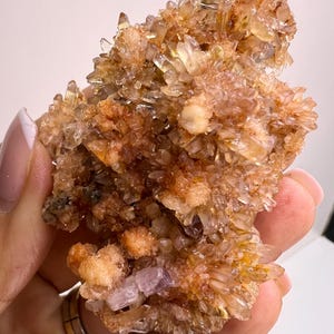May include: A cluster of small, translucent, orange-brown crystals with a few purple crystals at the base. The crystals are clustered together in a rough, natural formation.