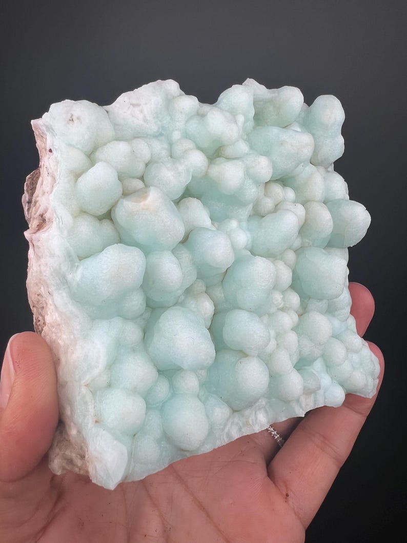 Op de afbeelding: Een groot, lichtblauw en wit, bubbelig mineraalmonster. Het monster heeft een ruw, getextureerd oppervlak.