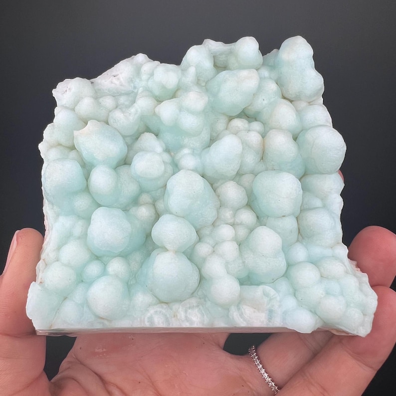 Op de afbeelding: Een cluster van lichtblauwe, bubbelvormige, minerale formaties. Het minerale exemplaar heeft een ruw, getextureerd oppervlak.