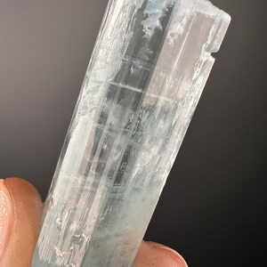 May include: A clear, light blue aquamarine crystal with a faceted, rectangular shape. The crystal is translucent and has a slight shimmer.