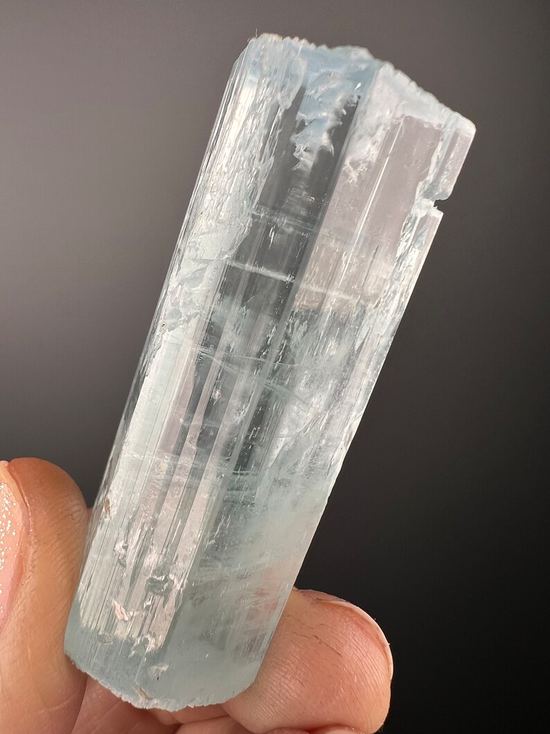 May include: A clear, light blue aquamarine crystal with a faceted, rectangular shape. The crystal is translucent and has a slight shimmer.