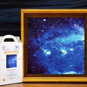 Pode incluir: Uma impressão emoldurada de uma galáxia azul profunda com nebulosas brancas e azul claro. A moldura dourada envolve a obra de arte. À esquerda, uma caixa branca com uma alça e as palavras "Distant Stars".