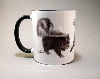 May include: White ceramic mug with a black handle. The mug features a black and white illustration of a skunk.