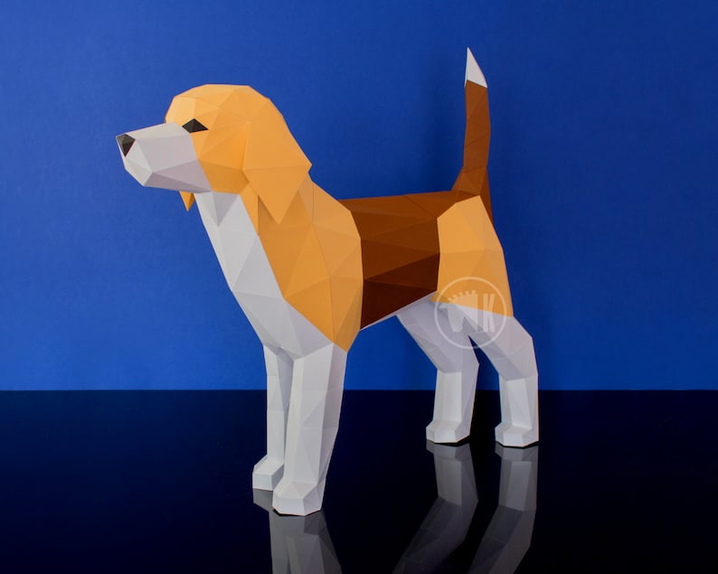 May include: A papercraft model of a beagle dog. The dog is standing on a black surface with a blue background. The dog is made of white, brown, and orange paper.